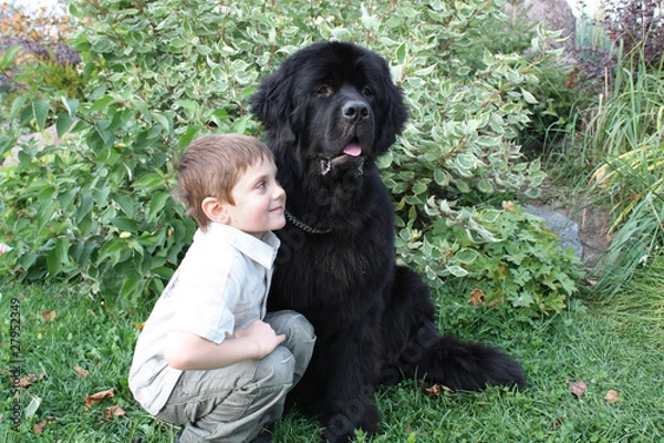 Obraz Мальчик в обнимку с черным ньюфаундлендом на фоне зелени