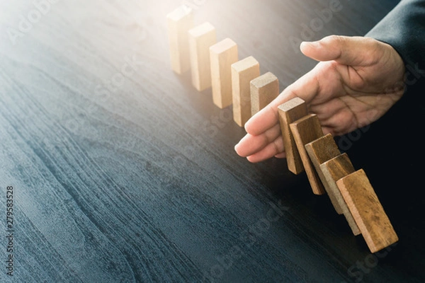 Fototapeta Close up of businessgirl hand Stopping Falling wooden Dominoes effect from continuous toppled or risk, strategy and successful intervention concept for business.