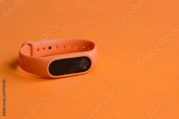 Fototapeta Orange fitness tracker on an orange background close up.