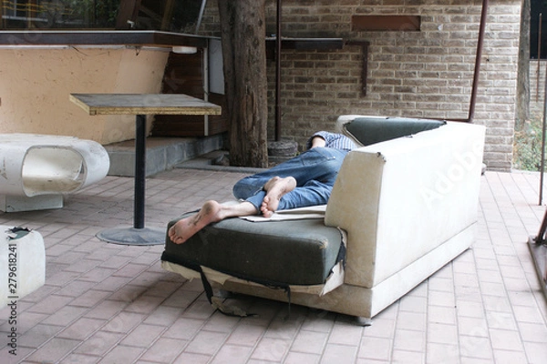 Fototapeta poor man lying on an old couch. poor man with dirty feet and no shoes