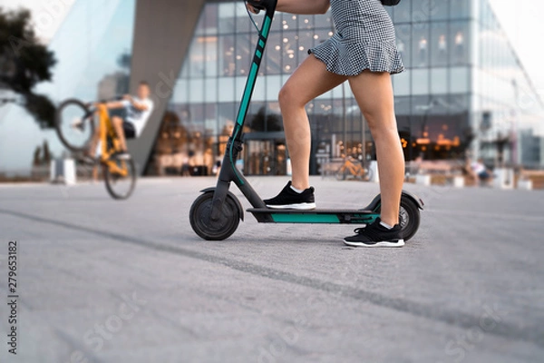 Fototapeta Unrecognizable woman, on e scooter in city environment 