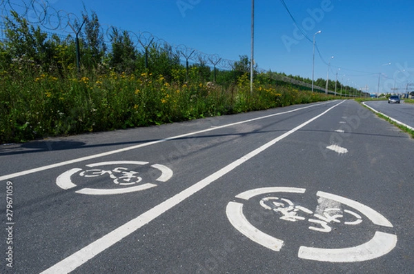 Fototapeta Two road signs "Bicycle path" on the asphalt and white lines close-up in the background of the blue sky