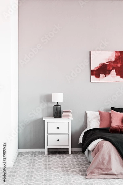 Fototapeta Lamp on white bedside table next to comfortable king size bed with pillows and blanket
