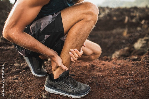 Fototapeta Achilles injury on running outdoors. Man holding Achilles tendon by hands close-up and suffering with pain. Sprain ligament or Achilles tendonitis.