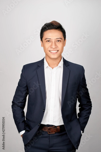 Fototapeta A young Asian man in suit put both hands in his pants pocket, isolated on a white background.