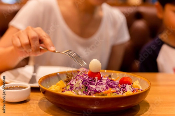 Fototapeta Woman hand with fork eating salad with tomato and quail egg in a plate.