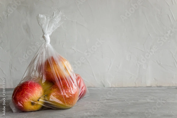 Obraz Fresh natural fruit in plastic bag on grey background. The concept of harm of food storage in artificial packages.