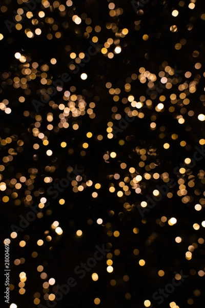 Fototapeta Blurry golden and white fairy lights in dark night creating beautiful bokeh effect with glowing circles or shiny dots, abstract image for Christmas or holiday card, banner or background