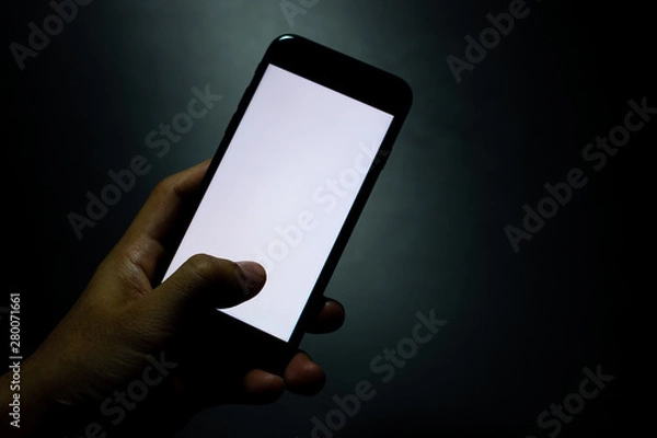 Obraz silhouette hand holding and touching a mobile phone with blank wihte screen in the dark darkness against dark blue background
