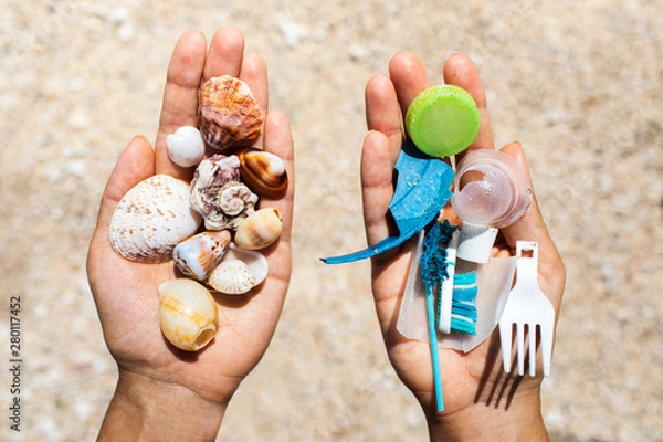 Fototapeta Concept of choice: save nature or continue to use disposable plastic. One hand holding beautiful shells, in the other - plastic waste. Beach sand on background. Environmental pollution problem.