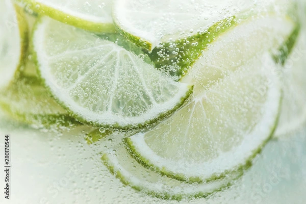 Fototapeta Close-up fresh lemon slices in cold lemonade with bubbles. Summer tropical beverage