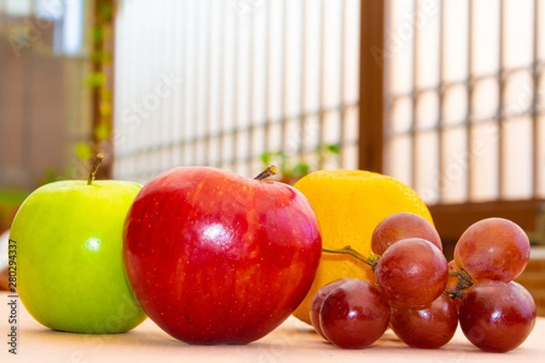 Fototapeta Green and red apples next to an orange and some grapes