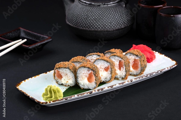 Obraz Closeup set of tempura fried sushi rolls with Philadelphia cheese, rice, salmon with chopsticks and soy on black background. Sushi menu. Japanese food and green tea teapot, copy space.