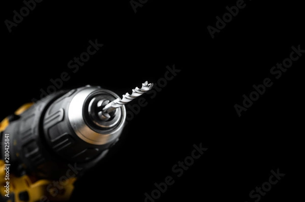 Fototapeta Electric drill closeup on a black background with wood and drills. Electrical tools. Hand battery screwdriver.