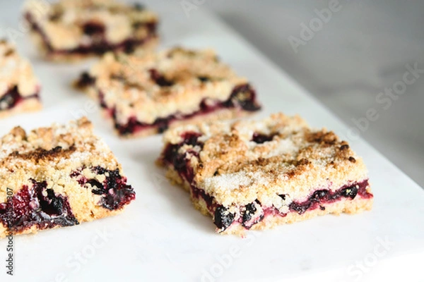 Fototapeta Honeysuckle crumble cake sliced into pieces on grey marble tray. Homemade streusel berries pie.  Selective focus. Haze effect