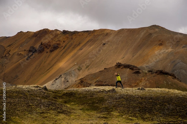 Fototapeta Beautiful woman is moving purposefully in front of mountain. Cloudy background. Landmannalaugar, Iceland