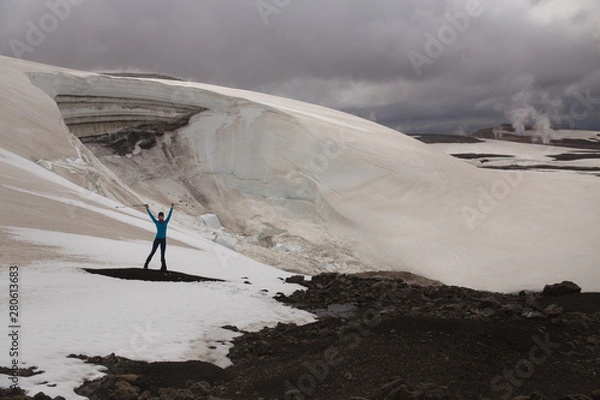 Fototapeta Beautiful woman is standing in front of many broken crevasses and fins of an icefall. Beautiful landscape with steam columns and dramatic sky background. Landmannalaugar, Iceland