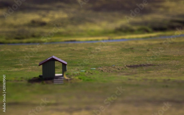 Fototapeta View of the small house on a green field with river on background. Tilt-Shift effect of the house with pass-through door. Landmannalaugar, Iceland