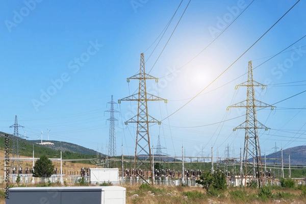 Fototapeta Electricity transmission pylons against blue sky. High voltage electricity poles with wind turbines.