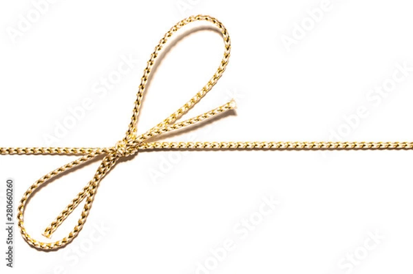 Fototapeta Golden satin rope parallel to frame with knotted bow gift ribbon wrap for Christmas present with intricate shine details isolated cut out top view on simple plain white background.
