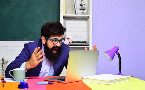 Fototapeta Education, tutoring and teacher concept. Male university student works with laptop in classroom. Student in glasses learning in auditorium. Teacher job. Profession, learning, knowledge. High school.
