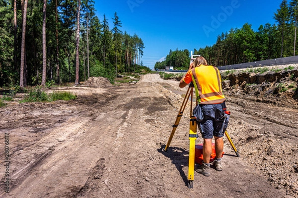 Obraz Surveyor engineer (worker) with equipment (theodolite or total positioning station) on the construction site of the road or highway