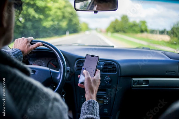 Fototapeta A man use smartphone while driving in the car. Road danger concept