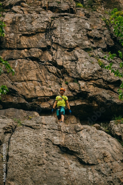 Fototapeta Low angle view of man throwing rope from the cliff against brown cracked rock