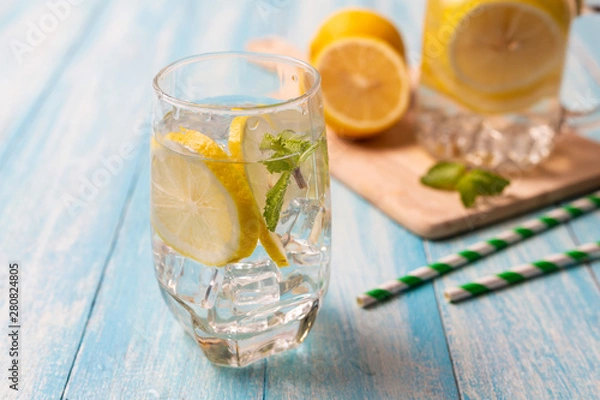 Fototapeta Fresh lemonade with lemon in glass on wooden background