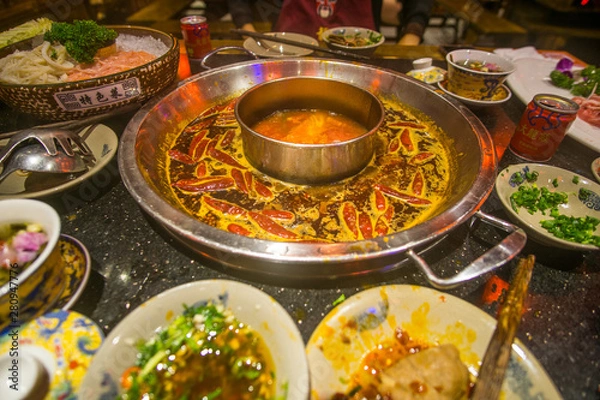 Fototapeta Sichuan Hot Pot in China a boiling spicy sauce and a table full of ingredients such as beef , fish and vegetables.  