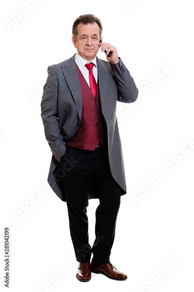 Fototapeta Full body portrait of handsome confident caucasian mature businessman 55-60 years old in grey tuxedo and red vest. Rich senior man talk by phone and looking to camera on isolated white background