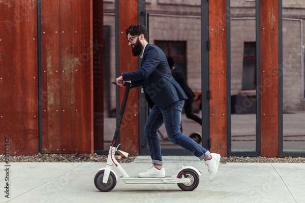 Fototapeta Bearded businessman riding to work on electric scooter