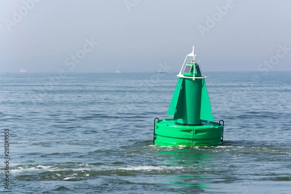 Obraz View on a green buoy in the sea, a device to safeguard ships and boats. It shows the way through the water, so that safety comes first.  It is a floating navigation device, with a solar cell on top