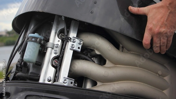 Fototapeta A man's hand open the hood of a powerful boat outboard motor, repair and maintenance of watercraft engines, a view of the intake manifold of a four cylinder four stroke injector motor