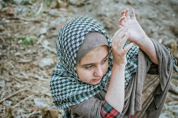 Fototapeta a refugee child in the war, a Muslim girl with a dirty face on the ruins, the concept of peace and war, the child is crying and waiting for help.