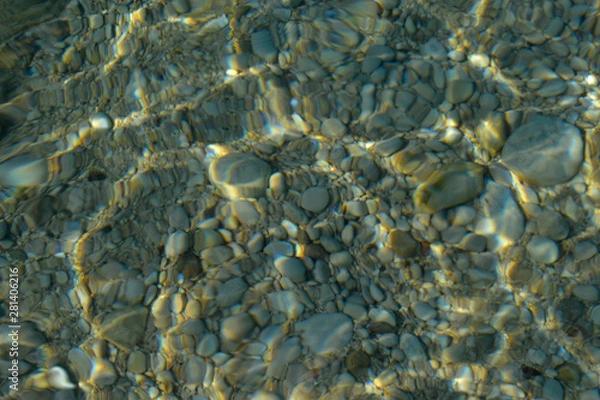 Fototapeta Top view of blue, green and turquoise colors of water, surface of sea on rocks and bottom. Reflection of sun beams in water, shallow soil, shoal of ocean. Sea texture, background, pattern, wallpaper.