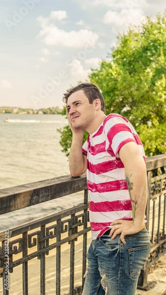 Fototapeta Portrait man near river on sunny day. Beautiful man posing by the sea on the waterfront