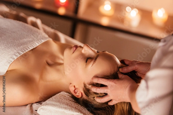 Obraz Hands of the masseuse make a manual massage of the head to a beautiful client woman. Concept of scalp treatment and hair growth stimulation