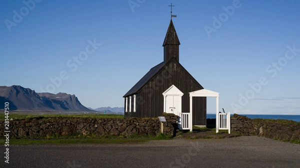 Obraz Black Church in Budir - PoI in western Iceland. The wooden church seen in late evening sun illumination slightly from the side. Its front and left side visible, ocean and mountains in background