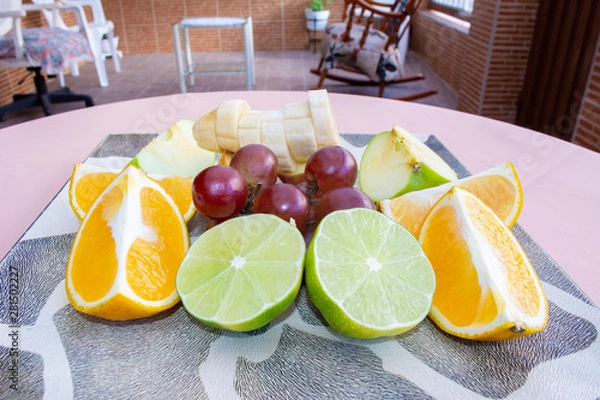 Fototapeta Orange, banana, lemon, apple and grapes, slices on top of a plate