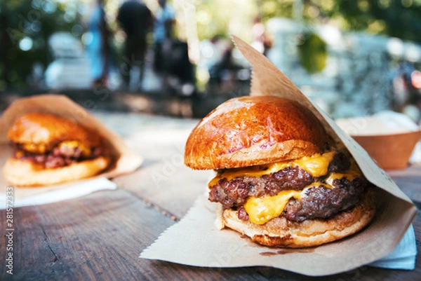 Fototapeta Street food festival background. Burgers close-up on the wooden table and people shown with a low-depth of field.