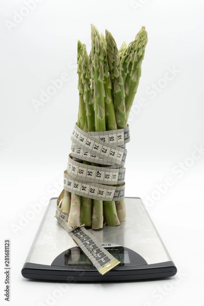 Fototapeta Asparagus surrounded by a medical tape on weighing scale for diets