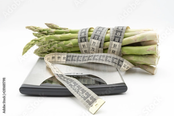Fototapeta Asparagus surrounded by a medical tape on weighing scale for diets