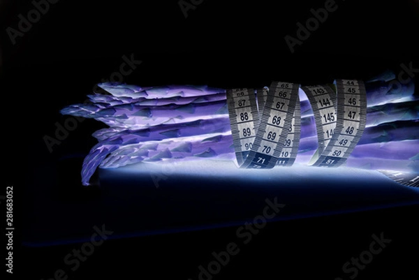 Fototapeta Asparagus surrounded by a medical tape on weighing scale for diets