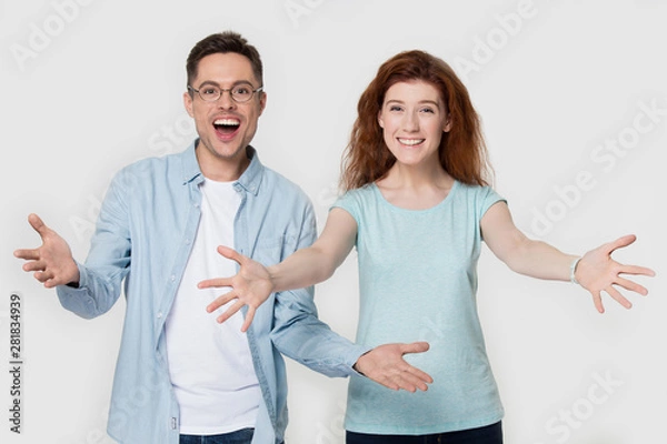 Obraz Excited couple looking at camera raise hands welcoming greeting gesture