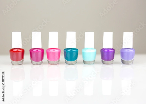 Fototapeta Group of bright multicolor nail polishes in a raw with reflection on a white table