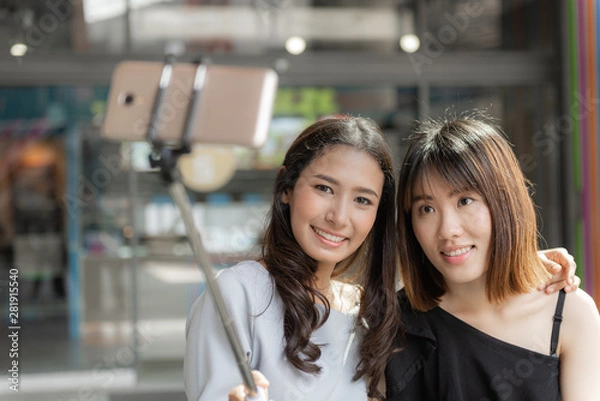 Fototapeta Portrait of cheerful two smiling girlfriends making a selfie at shopping mall.