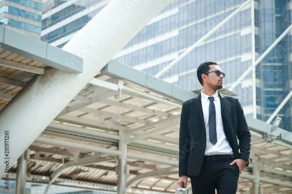 Fototapeta An Asian businessman holding a bag looking up at a tall building. Have space to write text