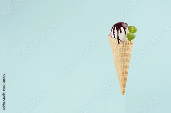 Fototapeta White creamy ice cream in crisp waffle cone with chocolate sauce, mint leaf on pastel green background, copy space.