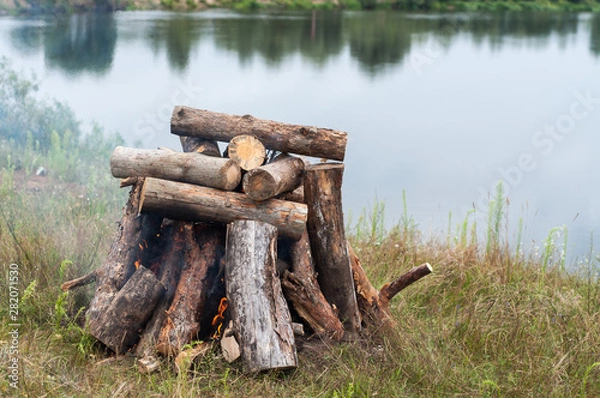 Fototapeta Warming stones at the stake for a sauna in nature. Bonfire of large logs on the banks of the river.